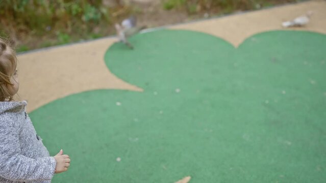 A young blonde girl plays on a colorful playground surface, conveying innocence and joy in an outdoor setting.
