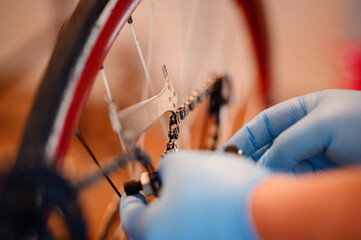 A mechanic using a tool to adjust a bicycle chain, focusing on the chain and rear wheel.