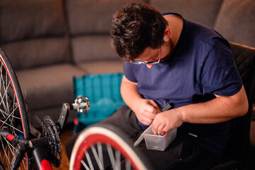 A man in casual attire repairs a bicycle indoors, using tools and focusing on small parts.