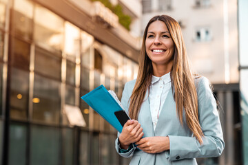 Smiling woman company CEO with file folder and cellphone in her hands on the way to work.