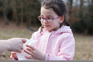 Sad little girl in glasses wipes her hands with a wet napkin in a winter snowless park