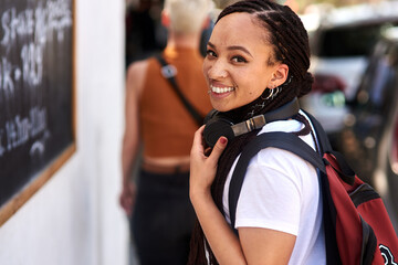 African woman, student and portrait in street with smile, backpack and headphones for music...