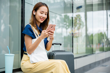 A woman sitting with her suitcase, using her mobile phone to send messages and stay connected while...