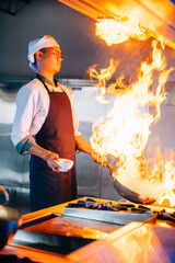 In professional kitchen chef hands handle flaming wok. Closeup of cooking expertise flames at work....