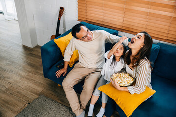 In warm atmosphere of their house smiling family bonds while watching TV with popcorn. father...