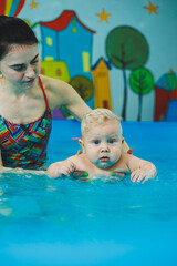 A little 8-month-old boy is learning to swim in the pool with a coach.