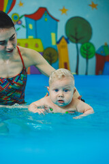 A little 8-month-old boy is learning to swim in the pool with a coach.