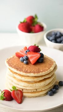 pouring syrup on piled pancake with strawberries and bluberries