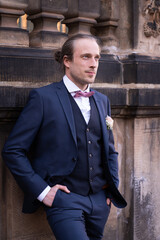 Portrait of the groom on his wedding day. Stylish, elegant groom stands on the steps and looks to...