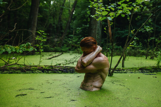 Redhead Man bare-chested athlete in a green swamp outside