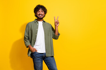 Portrait photo of young attractive hispanic guy in khaki shirt peacefully showing v sign isolated...