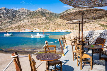 Small cafe bar with chairs and tables in Kamares bay port and mountains in background, Sifnos...