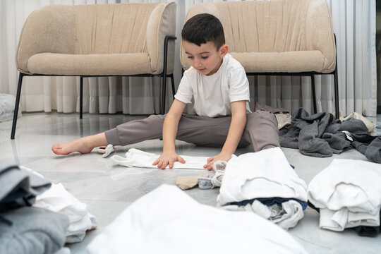Young Boy Sorting And Organizing Laundry on Tiled Floor at Home.
