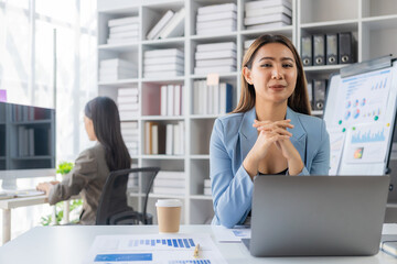 Two young Asian businesswomen work on laptop computers in the office with reports. Colleagues...