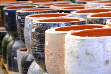 Rows of large ceramic pots wrapped in plastic for protection, displayed in a garden center.