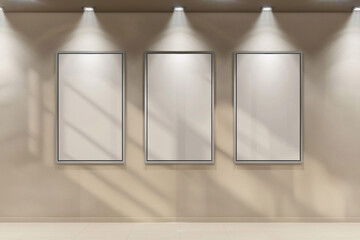 a minimalist setup with three empty posters in silver frames on a beige wall, with spotlights shining.