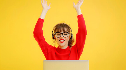 Happy woman with raised hands sitting in front of laptop with headphones and eyeglasses on isolated yellow background with space for copy