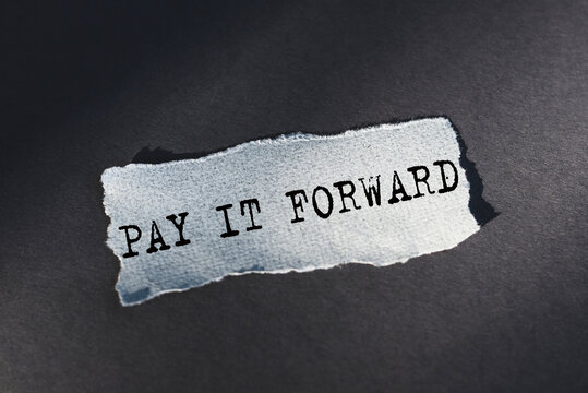 A torn piece of paper with the words pay it forward written on it, symbolizing the concept of doing good deeds for others without expecting anything in return.