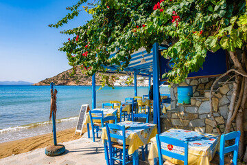 Blue chairs and tables in traditional Greek taverna restaurant on sandy beach in Platis Gialos...