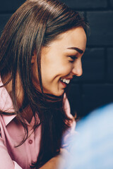 Cheerful brunette hipster girl laughing at jokes spending time with male colleague in coworking space, side view of happy young woman having fun during date sitting with boyfriend in cafe interior