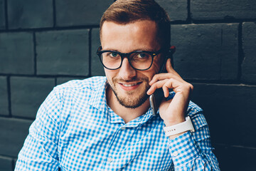 Portrait of smiling businessman noting information during phone conversation with colleague,positive male in spectacles talking with banking service operator writing in notepad looking at camera
