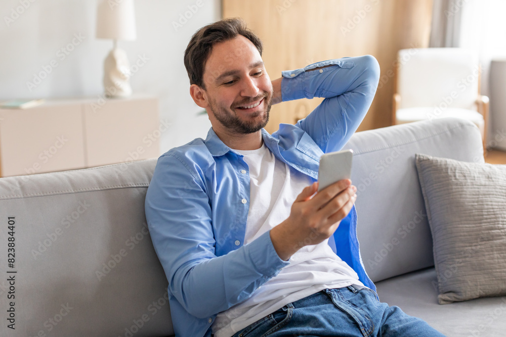 Poster a man is sitting on a couch indoors, engrossed in using his smartphone. he is focused on the screen,