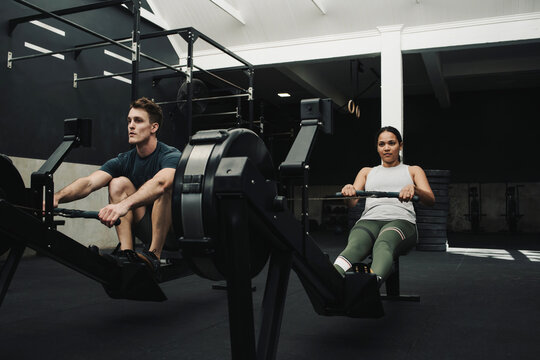 Strong athletes exercising while sitting on rowing machine in gym