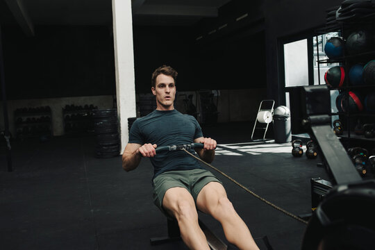 Strong man doing exercises while pulling rowing machine in gym