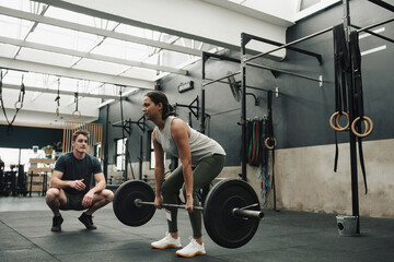 Strong sportswoman with trainer lifting barbell in gym