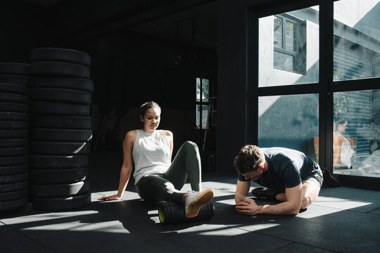 Fitness coach instructing sportswoman foam rolling calves