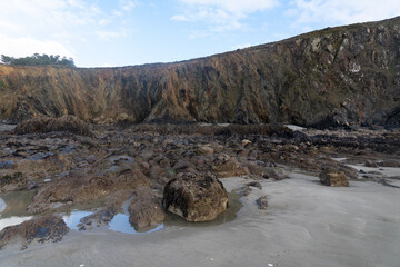 Plage de la presqu'île de Crozon, joyau breton baigné par la mer d'Iroise, avec sable fin, ses rochers aux pieds des falaises, et un ciel légèrement couvert.