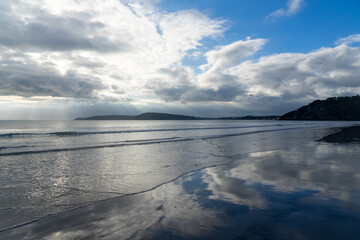 Plage sauvage de la presqu'île de Crozon, joyau breton baigné par la mer d'Iroise, avec sable fin et falaises, où les reflets du bleu du ciel et le blanc des nuages se posent sur le sable mouillé.