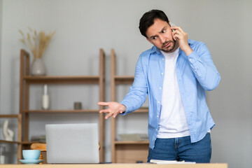 A man stands in his home office, with shelves in the background, gesturing with his hand while...
