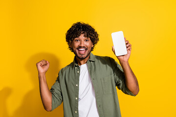 Photo portrait of young arabian student guy enjoy winning bet holding smartphone touchscreen isolated on yellow color background