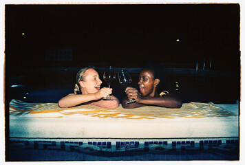 Girls clinking glasses with wine and laughing in pool