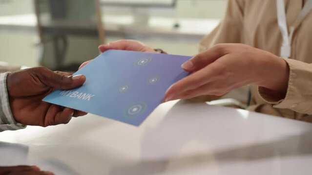 Medium close up of hands of male client taking blue envelope with credit card from manager when visiting bank office