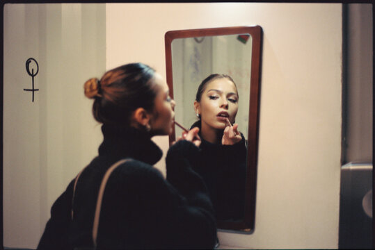 Young woman applying lipstick at home