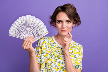 Portrait of pretty young woman hold cash think wear t-shirt isolated on purple color background