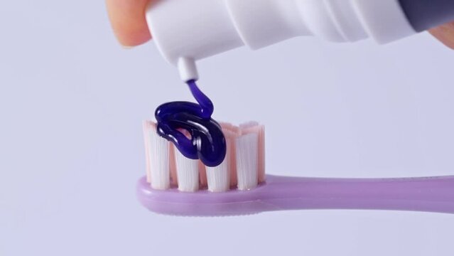 Pouring a whitening purple toothpaste on a toothbrush on white background. Texture of purple tooth gel for whitening teeth.