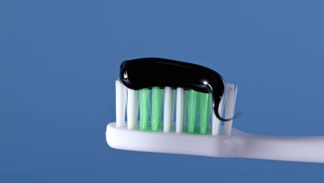 Charcoal toothpaste on toothbrush over blue background. Applying a swatch of black charcoal whitening toothpaste on brush.
