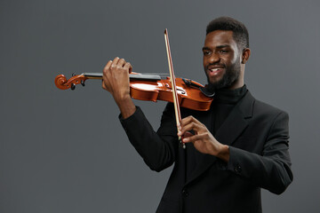 Professional African American male musician in elegant suit playing the violin on a neutral gray...