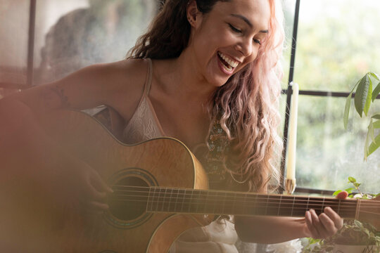 Beautiful woman with multicolored hair sitting at window with guitar