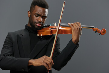 Professional African American musician performing classical music on violin in elegant black suit on gray background