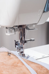 Modern sewing machine special presser foot with beige fabric and thread, closeup. Sewing process of sewing on a zipper. Business, hobby, handmade, zero waste, recycling, repair concept.