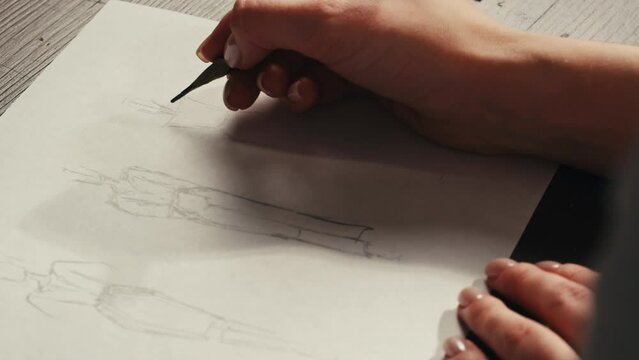 Young woman designer is drawing some clothes by pencil using ruler on white paper . The costume fashion designer making sketches for the work projects close-up. Drawing and sketching lessons