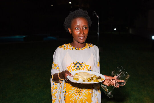 Black woman carrying plate with food and glasses