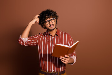 Photo of nice young man scratch head hold book wear striped shirt isolated on brown color background