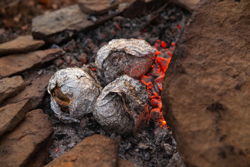 Juicy potatoes in silver foil are cooked over slow coals