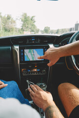 Cropped image of two tourists pointing right direction on display of modern online navigator in rental car sitting at helm during summer trip.Travellers choosing route on dashboard in vehicle