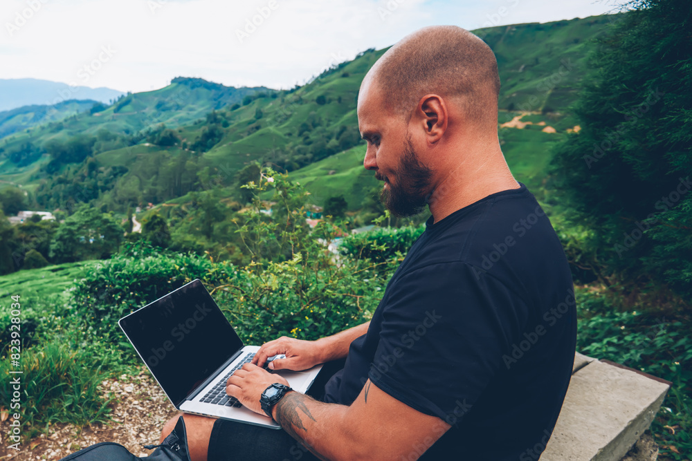 Poster pondering bearded tourist with netbook for remote work sitting in mountains while admiring scenery o